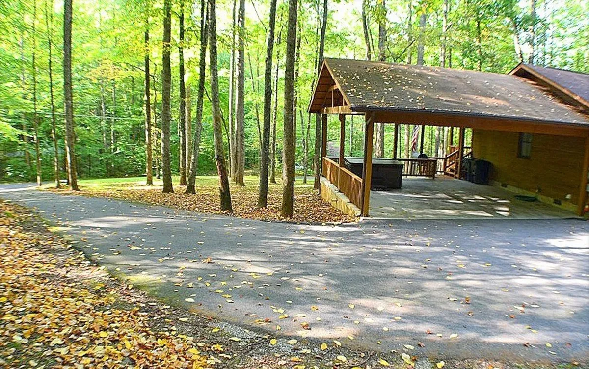 This exterior image features a welcoming wooden cabin set amidst a lush tree line, with a driveway leading up to a cozy porch area. The scene conveys an inviting and homey retreat, with natural surroundings that hint at outdoor adventures and relaxation after a day of activity.