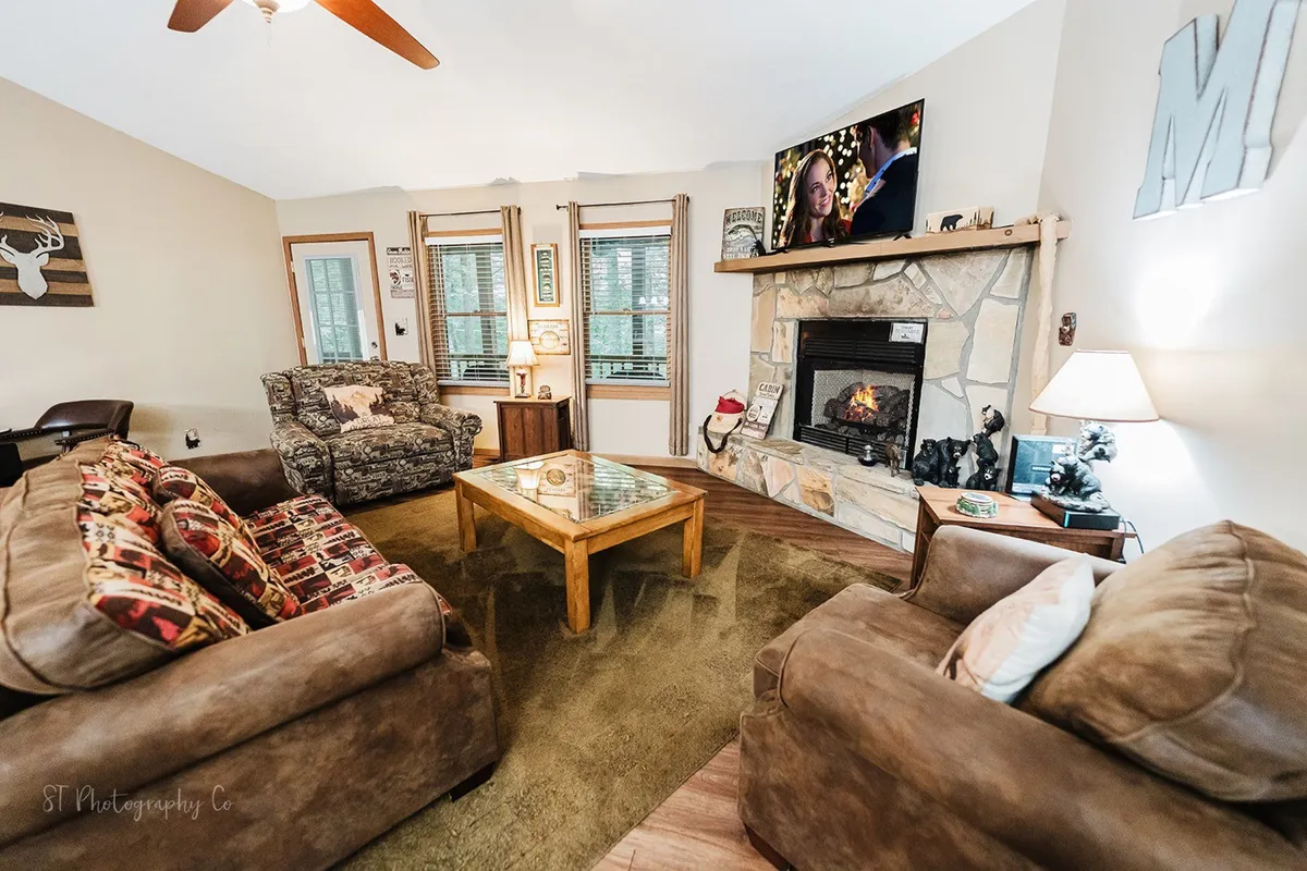 A cozy living room featuring a plush sofa facing a stone fireplace, a coffee table, and a television. The room is designed for comfort and relaxation, with warm, soft lighting and inviting decor that creates a homey atmosphere—ideal for both guests and their pets to unwind after outdoor adventures.