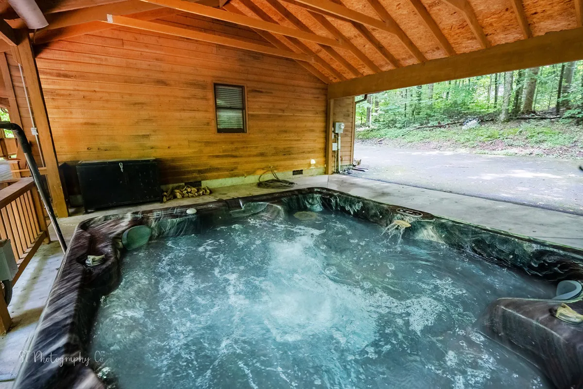 An inviting hot tub is set amidst wooden beams with glimpses of surrounding greenery, creating a tranquil space for unwinding. The setup suggests both family fun and relaxation, with nature just steps away.