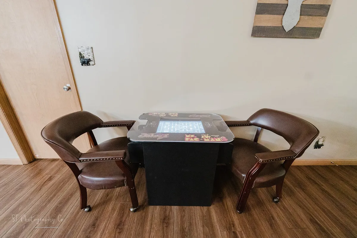 A cozy nook with two brown leather chairs and a small game table with a playful design, set against a warm backdrop. The intimate setup is perfect for game nights or quiet conversations, echoing the cabin’s atmosphere of connection and fun.